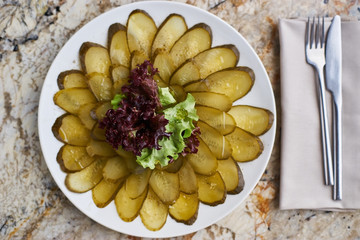 Slices ofmarinated cucumber on white plate. Knife and fork on textile napkin on marble table. Top view or flat lay.