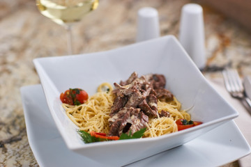 Beef stroganoff with spaghettini served in stylish square bowl on marble table