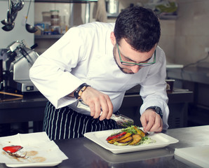 Chef in Restaurant garnishing vegetable dish, crop on hands, filtered image