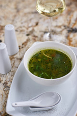 Minestrone soup with arugula served in a white bowl with ceramic spoon, glass of white wine on marble table