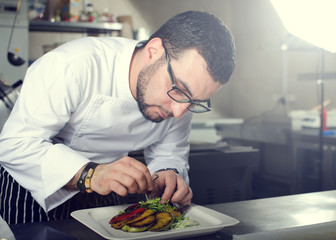 Chef in Restaurant garnishing vegetable dish, crop on hands, filtered image