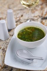 Minestrone soup with arugula served in a white bowl with ceramic spoon, glass of white wine on marble table