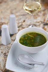 Minestrone soup with arugula served in a white bowl with ceramic spoon, glass of white wine on marble table