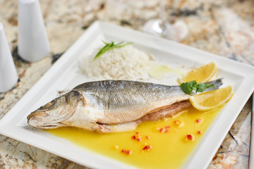 Whole boiled wolffish served with sauce from lemon butter and white wine on square white plate