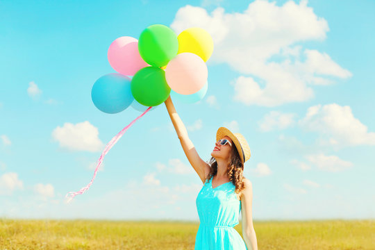 Happy smiling woman holds an air colorful balloons is enjoying a summer day on a meadow blue sky