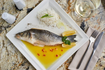 Whole boiled wolffish served with sauce from lemon butter and white wine on square white plate