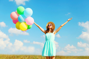 Obraz na płótnie Canvas Happy young smiling woman with an air colorful balloons is enjoying a summer day over blue sky meadow background