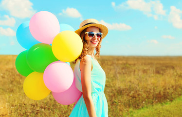 Portrait happy pretty smiling woman with an air colorful balloons is enjoying a summer day on a meadow blue sky