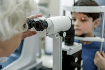Old female oculist verifying vision of child