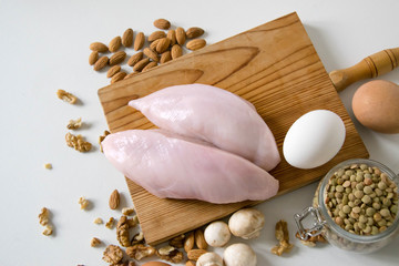 Raw food grocery full of proteins on wooden brown cutting rustic board on white table. Chicken fillet, eggs, mushrooms, lentils. Healthy sport diet background. Healthcare lifestyle or proteins concept