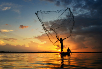 Silluate fisherman and boat in river on during sunrset,fisherman trowing the nets on during...