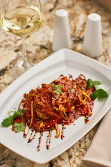 Spicy tofu served on white plate with glass of white wine on marble table. Vegeterian cuisine.