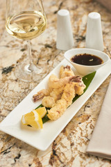 Japanese cuisine. Hot crispy prawn tempura served on white plate with soy sauce and glass of white wine.