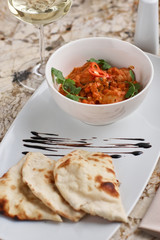 Chicken fillet slices fried in spicy cream sauce with tortilla bread served in white bowl with glass of wine, knife and fork on napkin on marble table