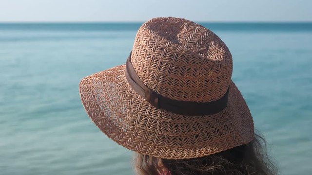Woman putting on beach hat. Person on blurred sea background. Sun protection tips.