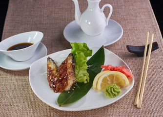 Japanese cuisine. Sashimi with baked eel fish served with soy sauce and chopsticks on table.