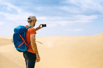 A tourist with a backpack takes photo of the desert by phone