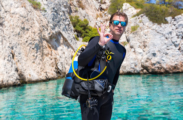 Junger Scuba Taucher mit Ausrüstung zeigt das OK Zeichen