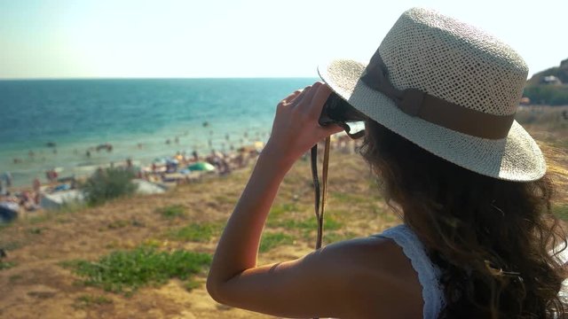Lady looking into binoculars, seaside. Young woman on outdoor background.