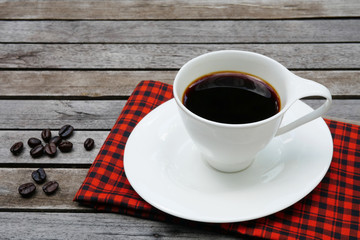 Cup of coffee with coffee beans and red handkerchief on wooden background