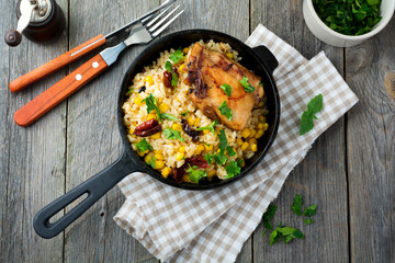 Rice with corn, soy sauce and fried chicken thigh on a cast-iron frying pan. Top view. Selective...