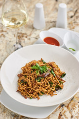 Flat egg noodles with duck meat, chicken, shiitake mushrooms served on white plate with white garlic and red spicy sauce