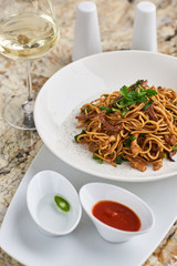 Flat egg noodles with duck meat, chicken, shiitake mushrooms served on white plate with white garlic and red spicy sauce