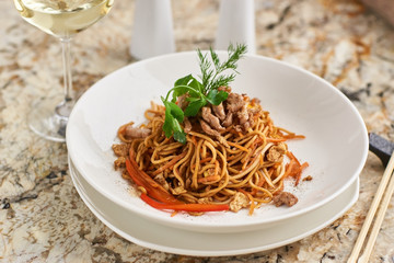 Flat egg noodles with pork slices served on white plate with white garlic and red spicy sauce