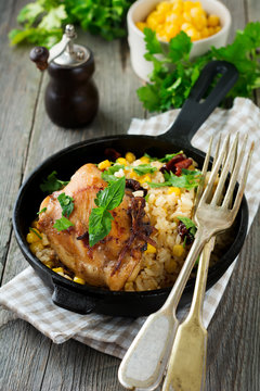 Rice with corn, soy sauce and fried chicken thigh on a cast-iron frying pan. Selective focus.