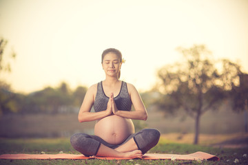 Naklejka na ściany i meble healthy pregnant woman doing yoga in nature outdoors.Vintage color
