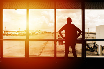 Silhouette of young man traveler looking outside of terminal window at airport before departure