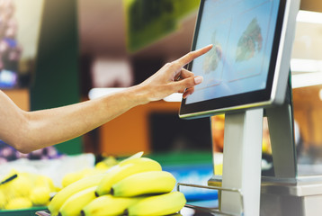 The buyer weighs the yellow bananas and points the fingers on the screen electronic scales, woman shopping healthy food in supermarket blur background, hands buy nature products in store grocery