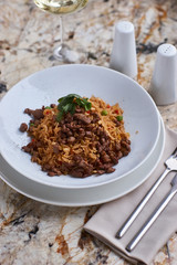 Fried rice with beef slices served in white round plate with glass of white wine on marble table
