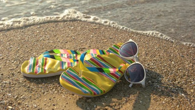 Sunglasses and flip flops, close up. Seashore under sunlight. Spend summer at tropical island.