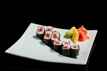 Sushi roll with fresh tuna fish with vasabi, pickled ginger and lemon slice on white plate on black background