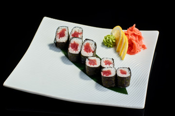 Sushi roll with fresh tuna fish with vasabi, pickled ginger and lemon slice on white plate on black background