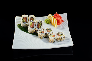 Sushi roll with fresh salmon and cucumber with vasabi, pickled ginger and lemon slice on white plate on black background