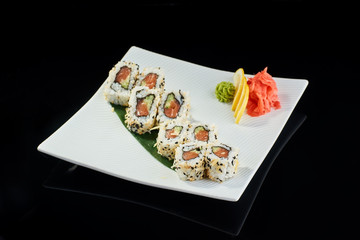 Sushi roll with spicy salmon with vasabi, pickled ginger and lemon slice on white plate on black background