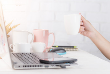 woman's hand holding a cup of coffee while sitting at office desk in front of laptop