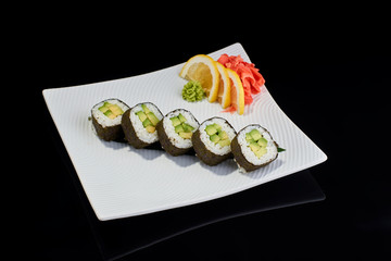 Vegeterian sushi roll with avocado with vasabi, pickled ginger and lemon slice on white plate on black background