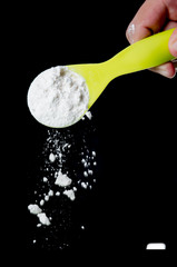 Pouring flour from the measuring spoon on black background