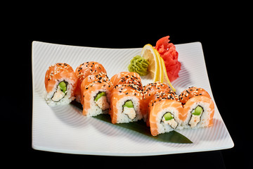 Sushi Roll with salmon and avocado served with vasabi, pickled ginger and lemon slice on white plate on black background