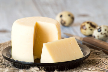  Cheese.   Round head of homemade cheese on a small plate on a burlap, next to quail eggs and a knife on a wooden table.