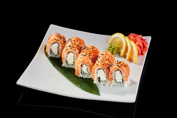 Sushi Roll Philadelphia served with vasabi, pickled ginger and lemon slice on white plate on black background