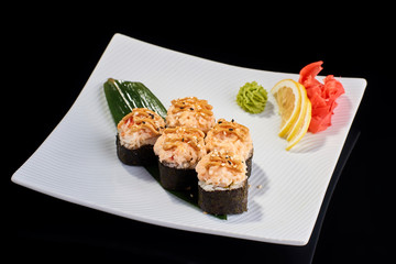Baked Sushi Roll with crab meat, salmon and avocado served with vasabi, pickled ginger and lemon slice on white plate on black background