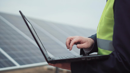 Outdoors crop shot of a person browsing the laptop on the solar panel site.