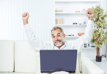 enthusiastic businessman with an open laptop sitting on sofa in modern office.