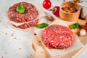 Fresh raw home-made minced beef steak burger with spices, tomatoes and basil, on a white stone concrete table, 