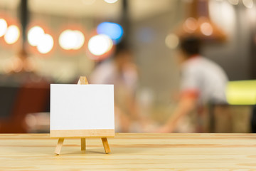 Easel with blank canvas on wooden table,billboard on wood desk top with supplied bokeh background,Template mock up for montage of display your product.vintage color