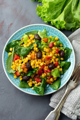  Warm salad with corn, pepper, olives and lettuce on a blue ceramic plate on a dark background. Selective focus.Top view.
